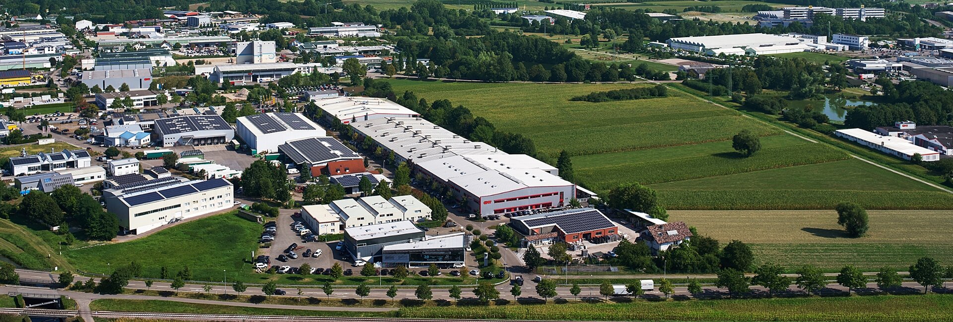 LucyLuftbild eines großen Industrie- oder Gewerbegebäudes mit angrenzenden}}\,\ legnagyobbsérie von Hallen und Verwaltungsgebäuden auf einem klimatisierten Gelände mit angrenzenden Grünflächen, Straßen und parkähnlichen Bereichen