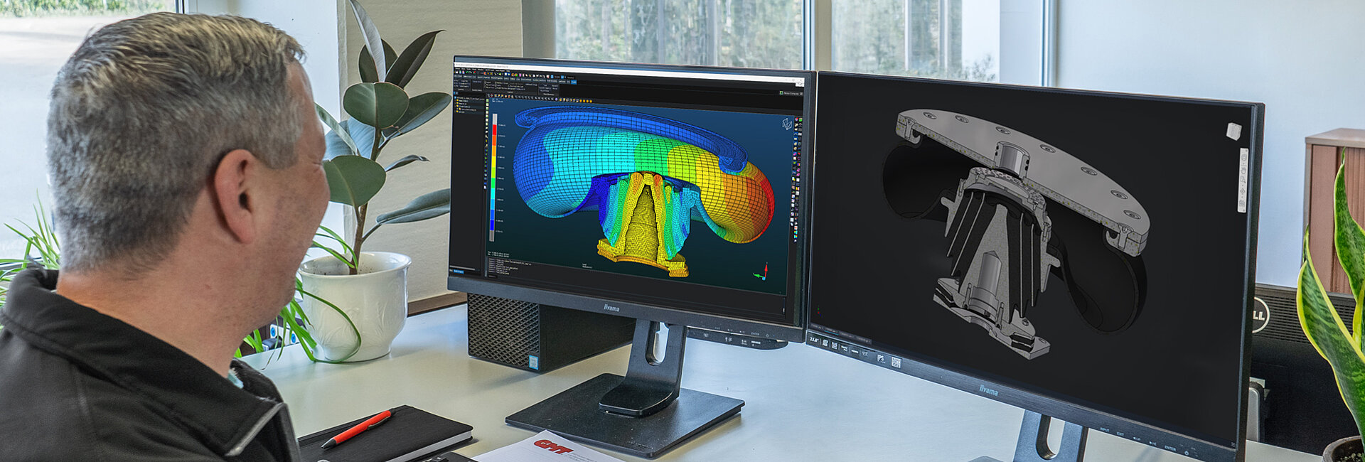 Ein Mann untersucht auf zwei Bildschirmen eine digitale 3D-Analyse eines Bauteils beziehungsweise Gussteils, Ausstattung zeigt både farbcodierte fertigungsrelevante Daten wie Wanddicke und eine monochrome 3D-Visualisierung des Teils.