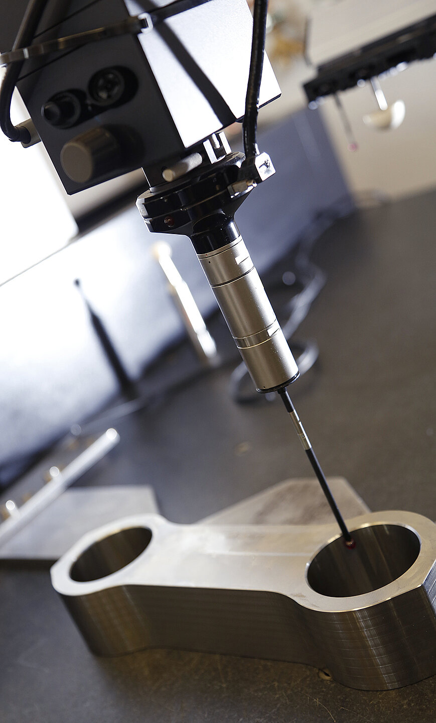 CNC Fräsmaschine bearbeitet eine-metal-l-beformte-Y-Stück-Verbindung mit Kreisf boh­rungen, montiert auf dunkler Arbeitsplatte inklusive Maschinenarm und Fräser.