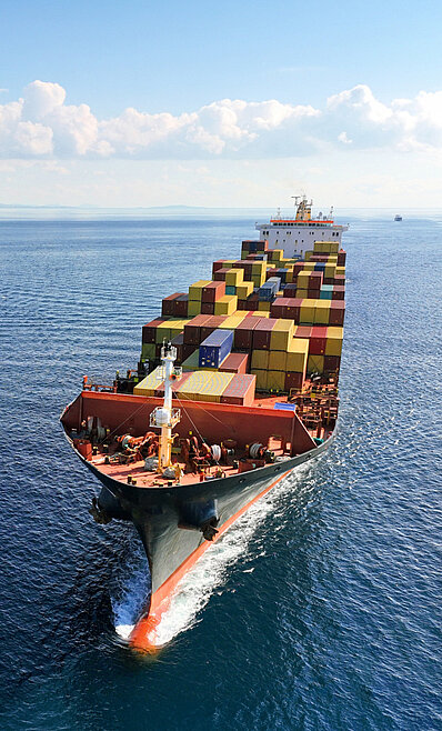 Großes Frachtschiff auf See bewegend, beladen mit zahlreichen farbenfrohen Frachtcontainern, fährt über tiefblaues, leicht welliges Meer, Blickwinkel von oben.
